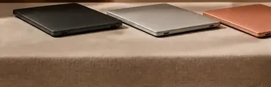 Several distinct closed laptops arranged in a row on a table, each a different colour